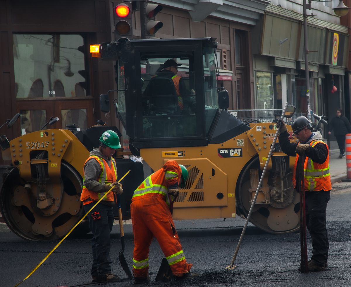 Road crew in high-visibility clothing working beside a roller.