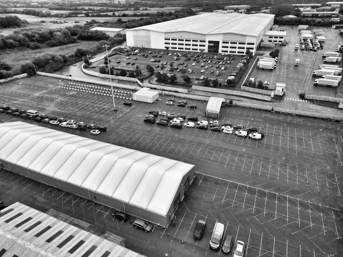 Aerial view of commercial buildings, parked vehicles and broad paved areas.