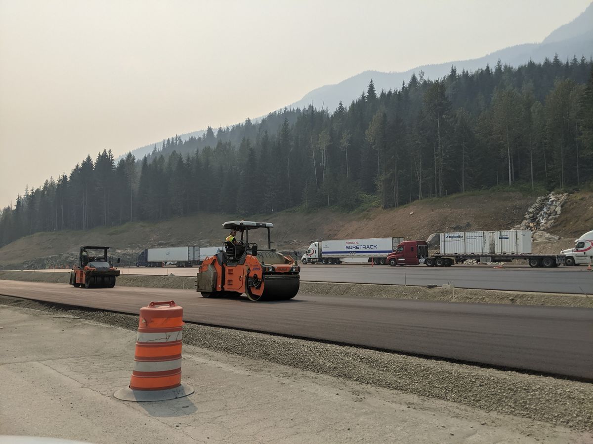 Road rollers beside a traffic barrel on an asphalt work site.