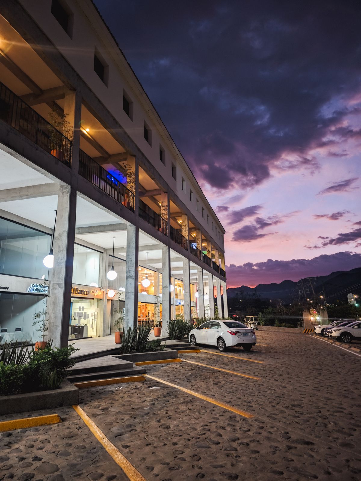 Retail storefronts and a marked parking area at dusk.