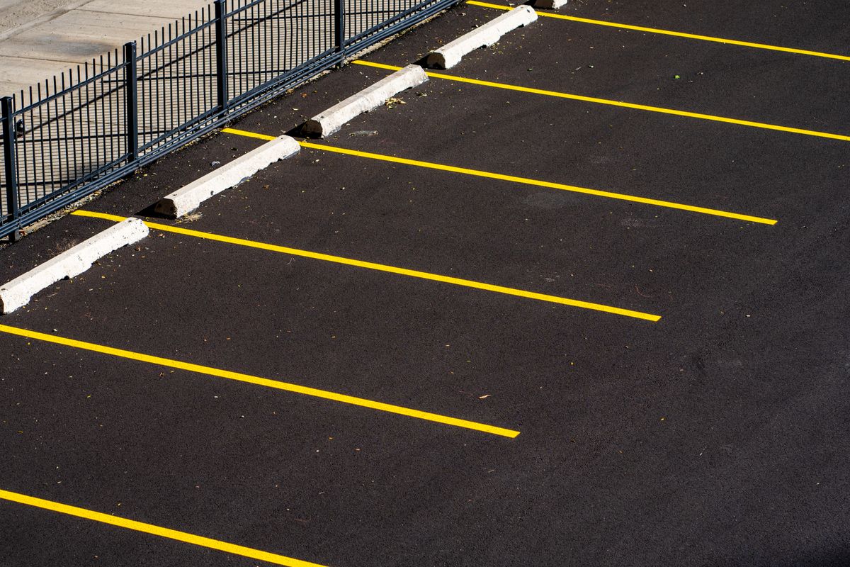 Yellow parking lines and wheel stops beside a metal fence.