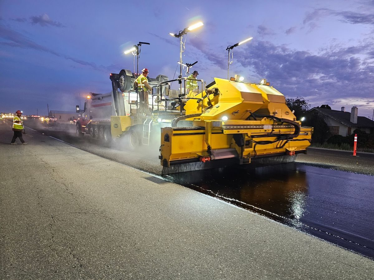 Illuminated road machine applying a surface treatment at dusk.