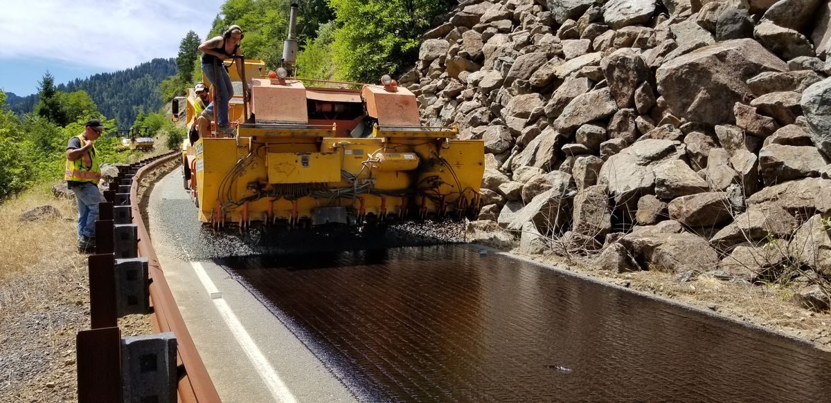 Paving equipment working along a road beside a rocky slope.