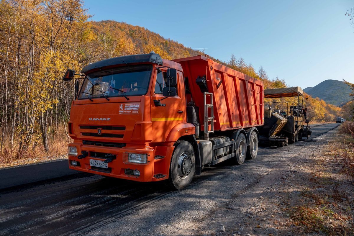 Orange dump truck and road equipment beside autumn trees.