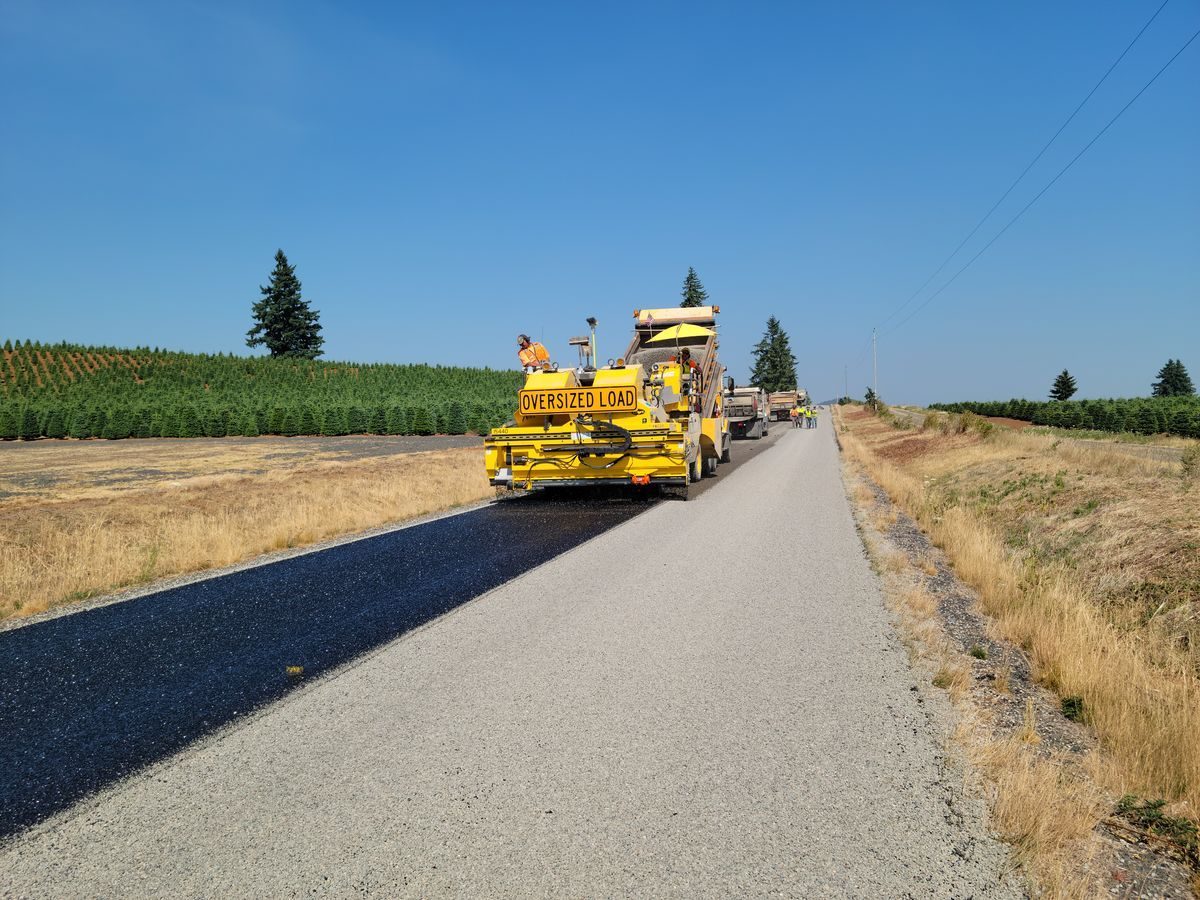 Yellow road machine working along a lane bordered by fields.