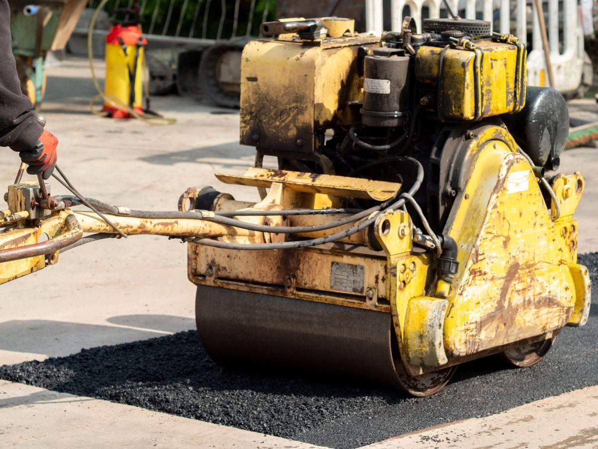 Compact road roller beside workers carrying out pavement repairs.