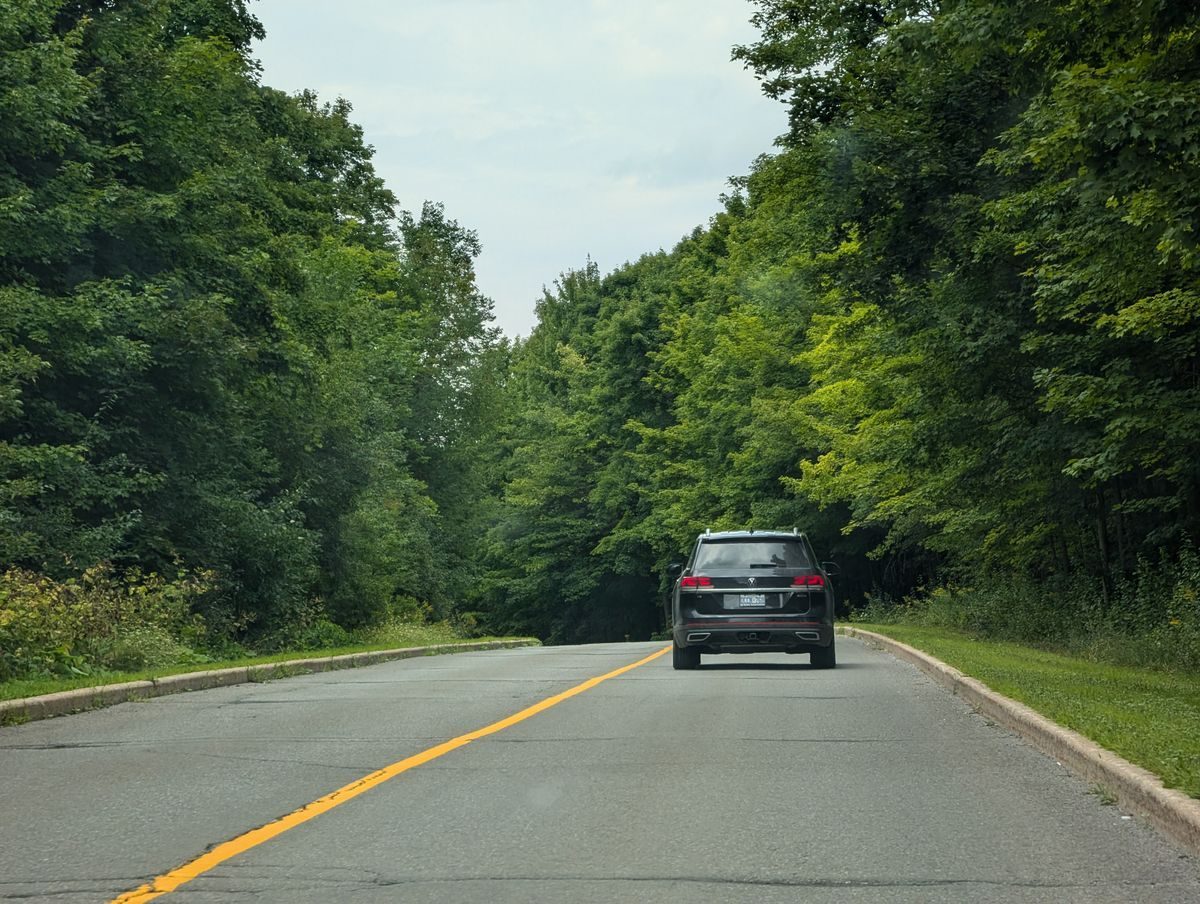 Car travelling along a marked asphalt road bordered by trees.