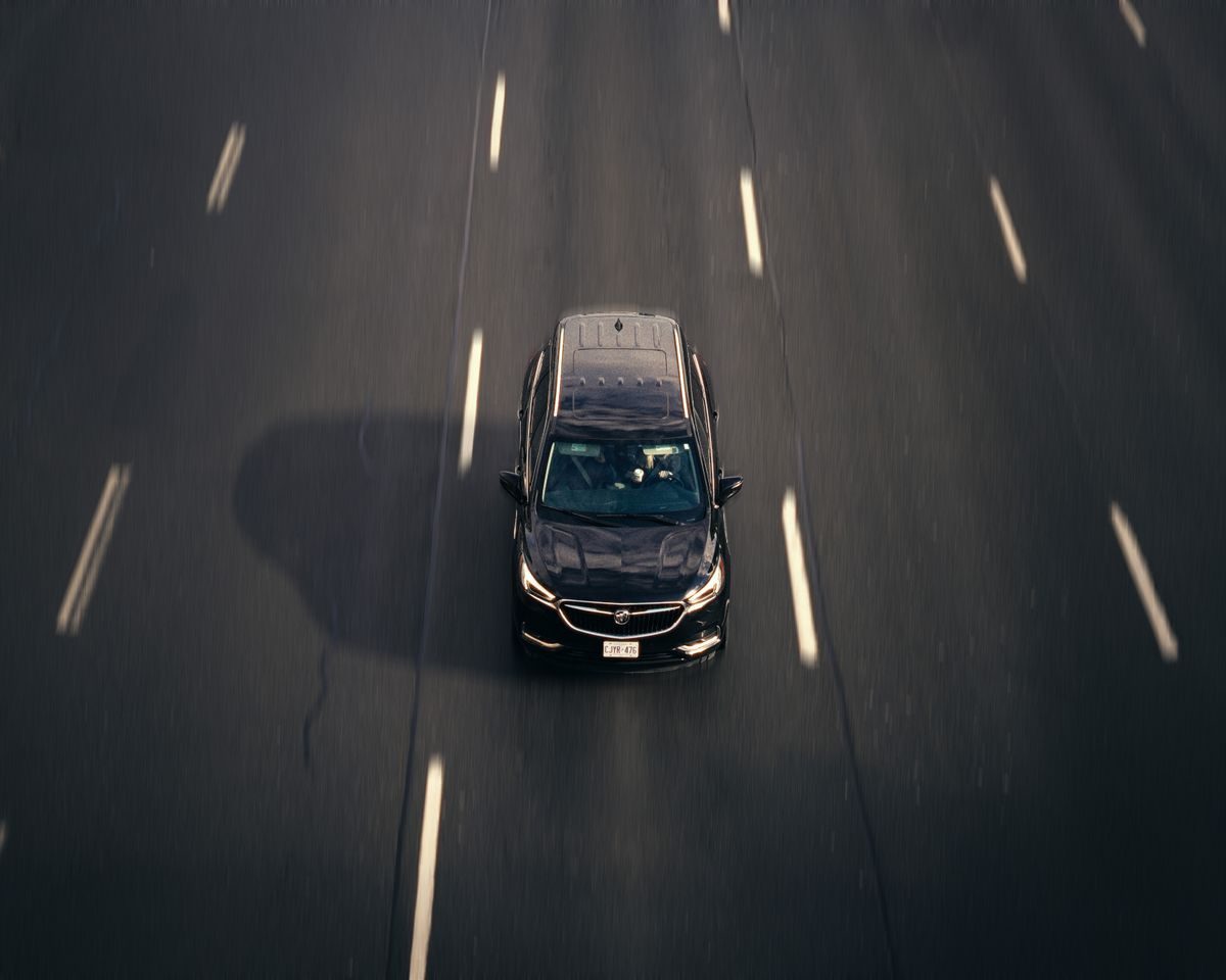 Overhead view of a car travelling between marked asphalt lanes.