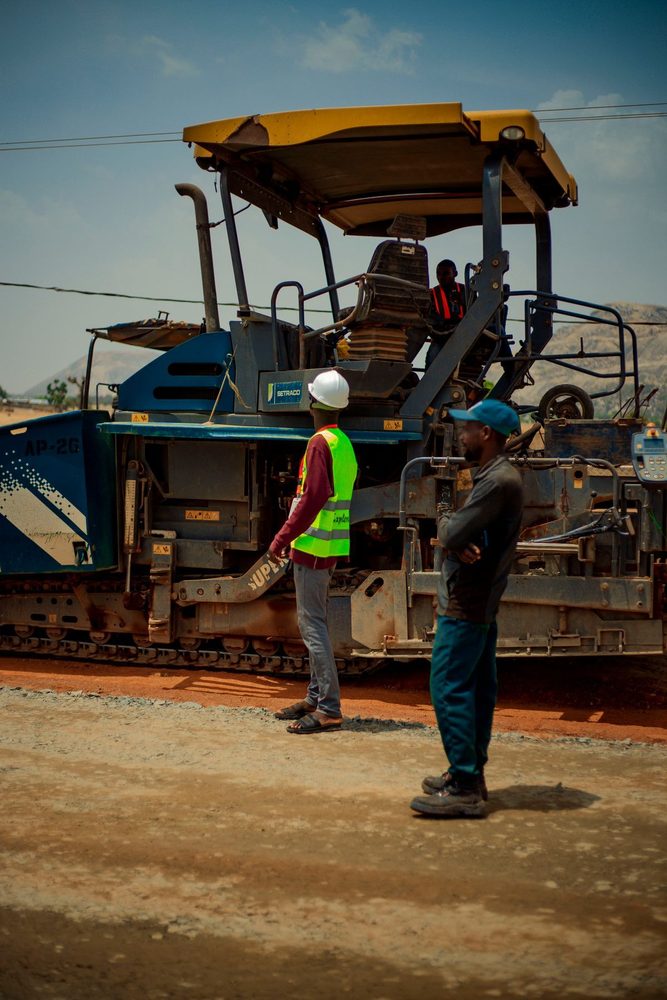 Two workers beside a large road paving machine.