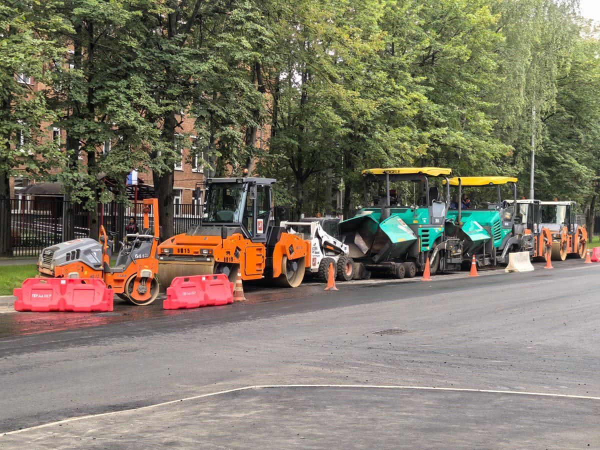 Road rollers and paving machines lined up beside an urban roadway.