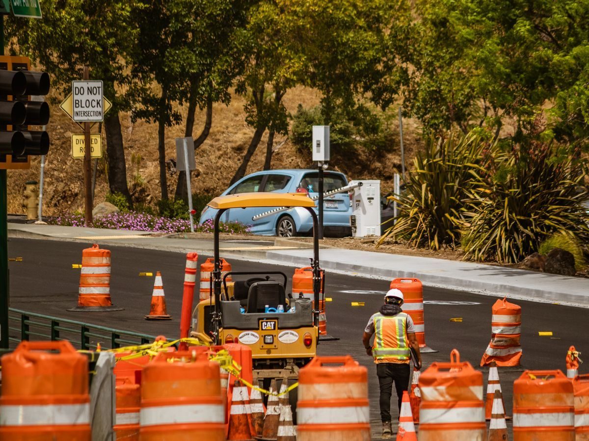 Road crew and compact roller inside a coned street work zone.
