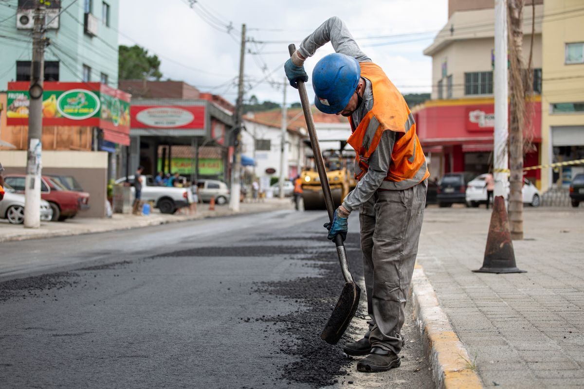 Worker finishing dark asphalt beside a street curb.