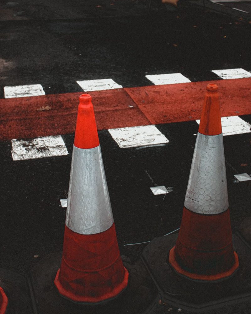 Traffic cones beside painted crossing lines on asphalt.