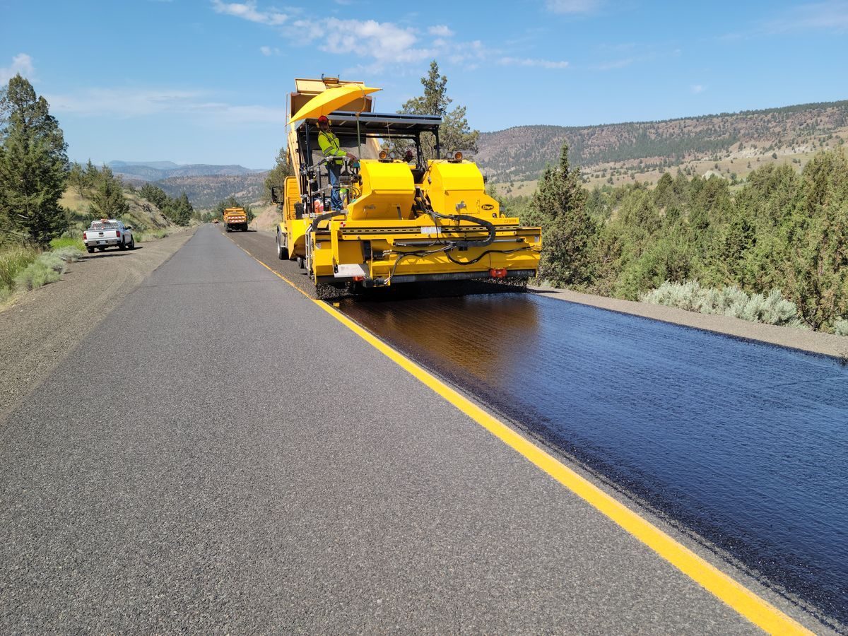 Road machine applying a dark surface treatment beside a yellow centre line.