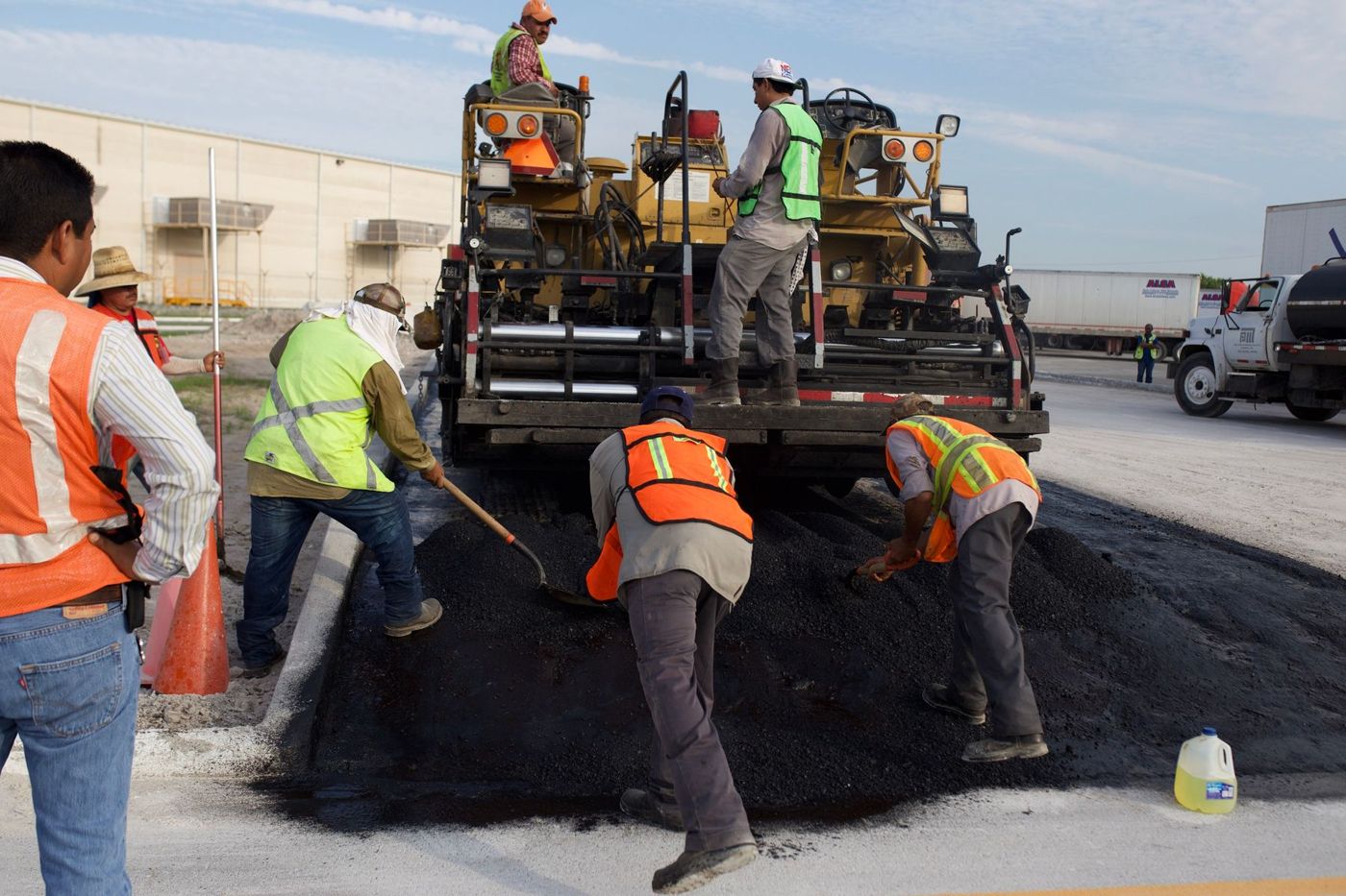 Road crew placing asphalt beside paving machinery.