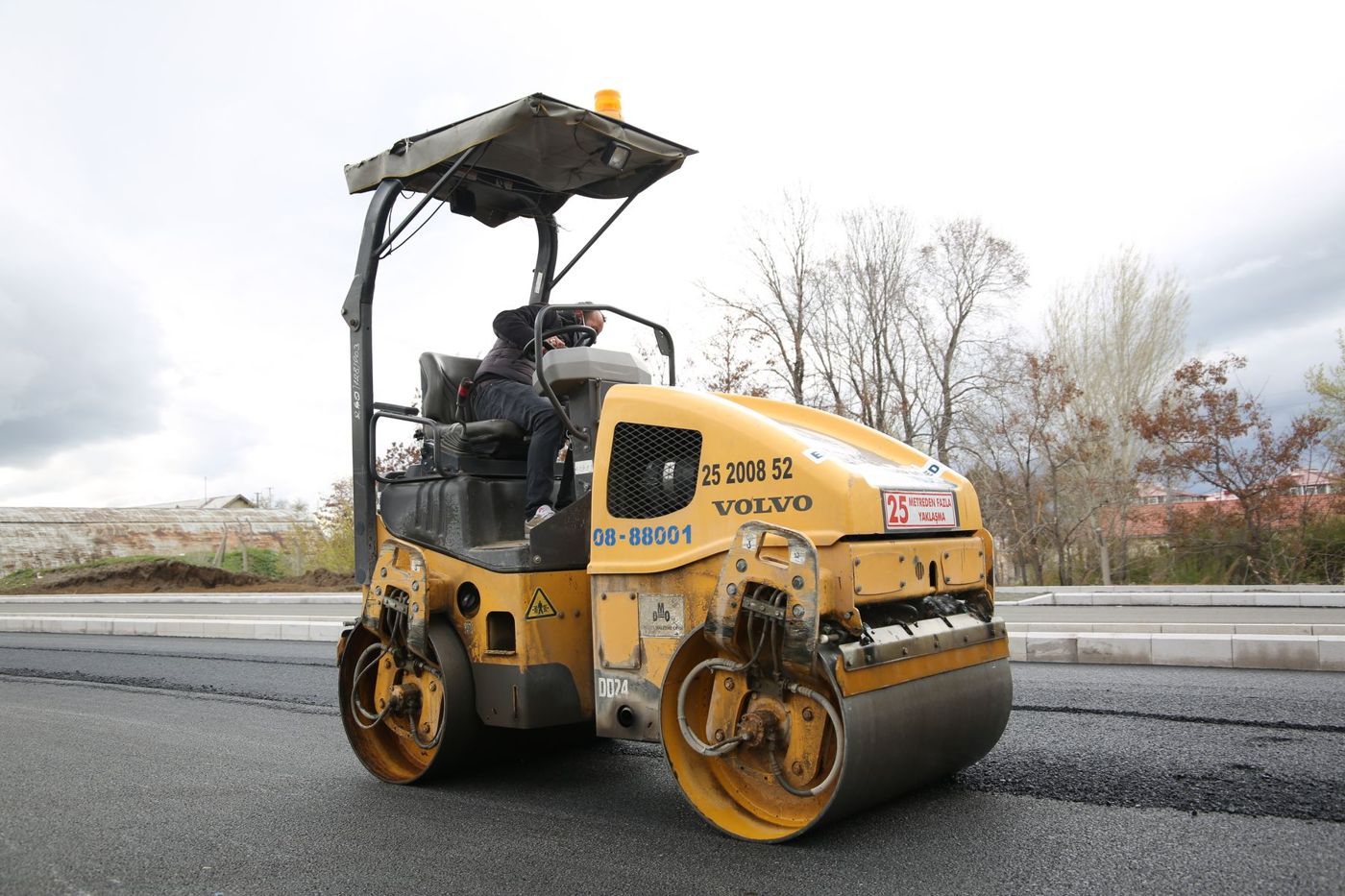 Road roller compacting asphalt along a roadway.