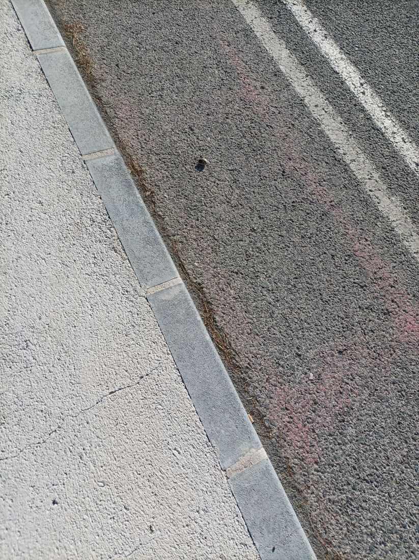 Concrete curb separating the sidewalk from asphalt roadway.