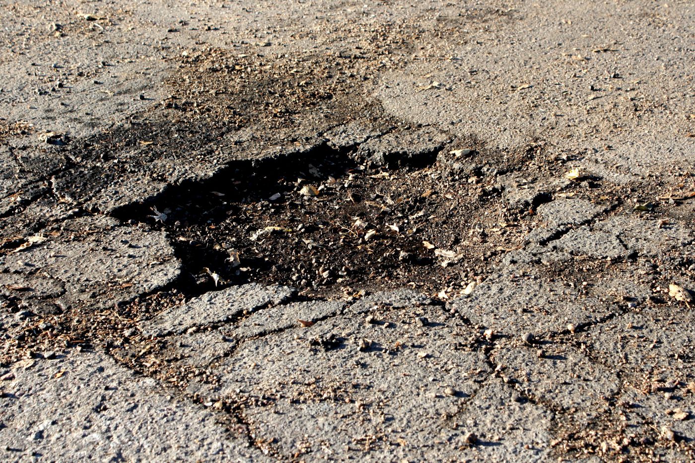 A pothole with broken asphalt edges in a roadway.